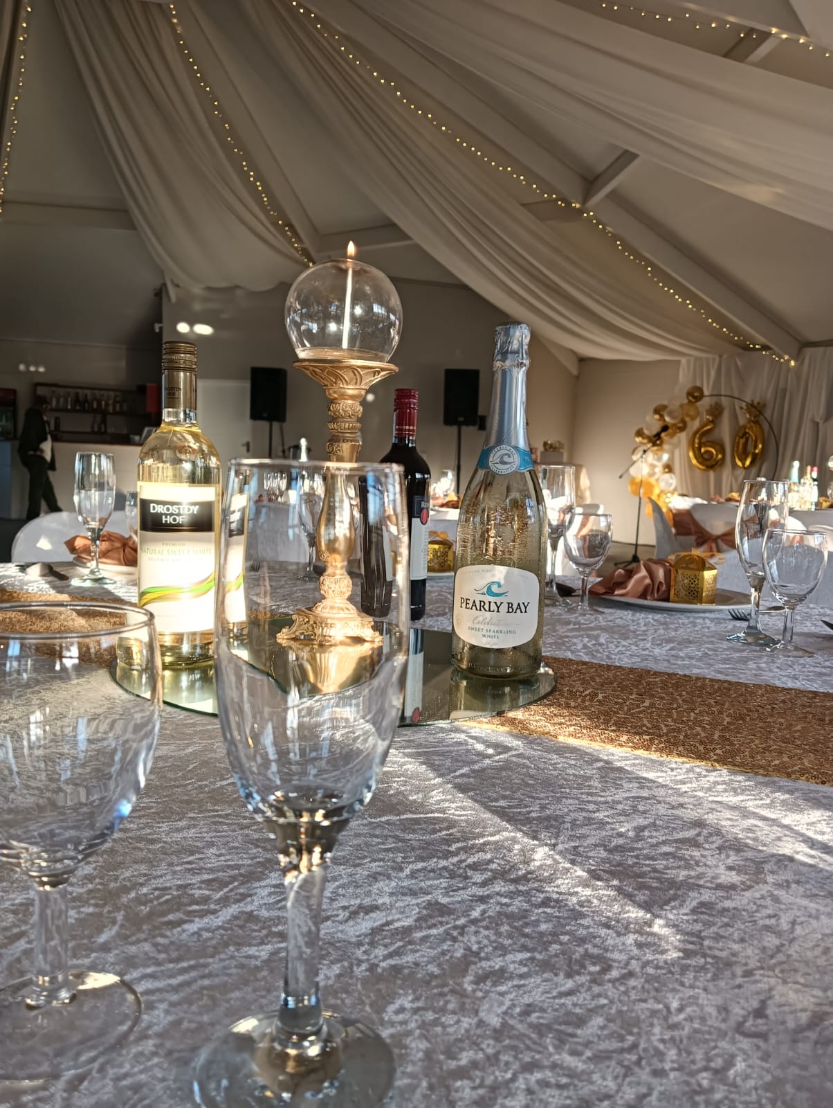 Elegant wedding reception table with sparkling glassware, wine bottles, candle centrepiece and white draped ceiling décor