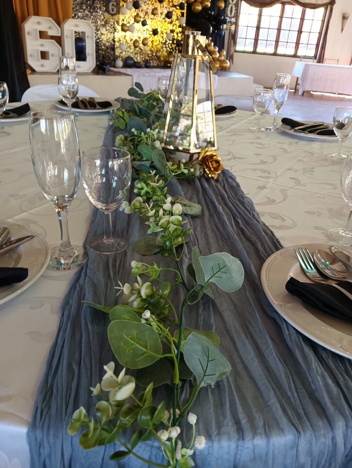 Elegant 60th birthday celebration table with blue table runner, greenery, gold lantern centerpiece and black napkins at Mayerskraal Wedding Venue