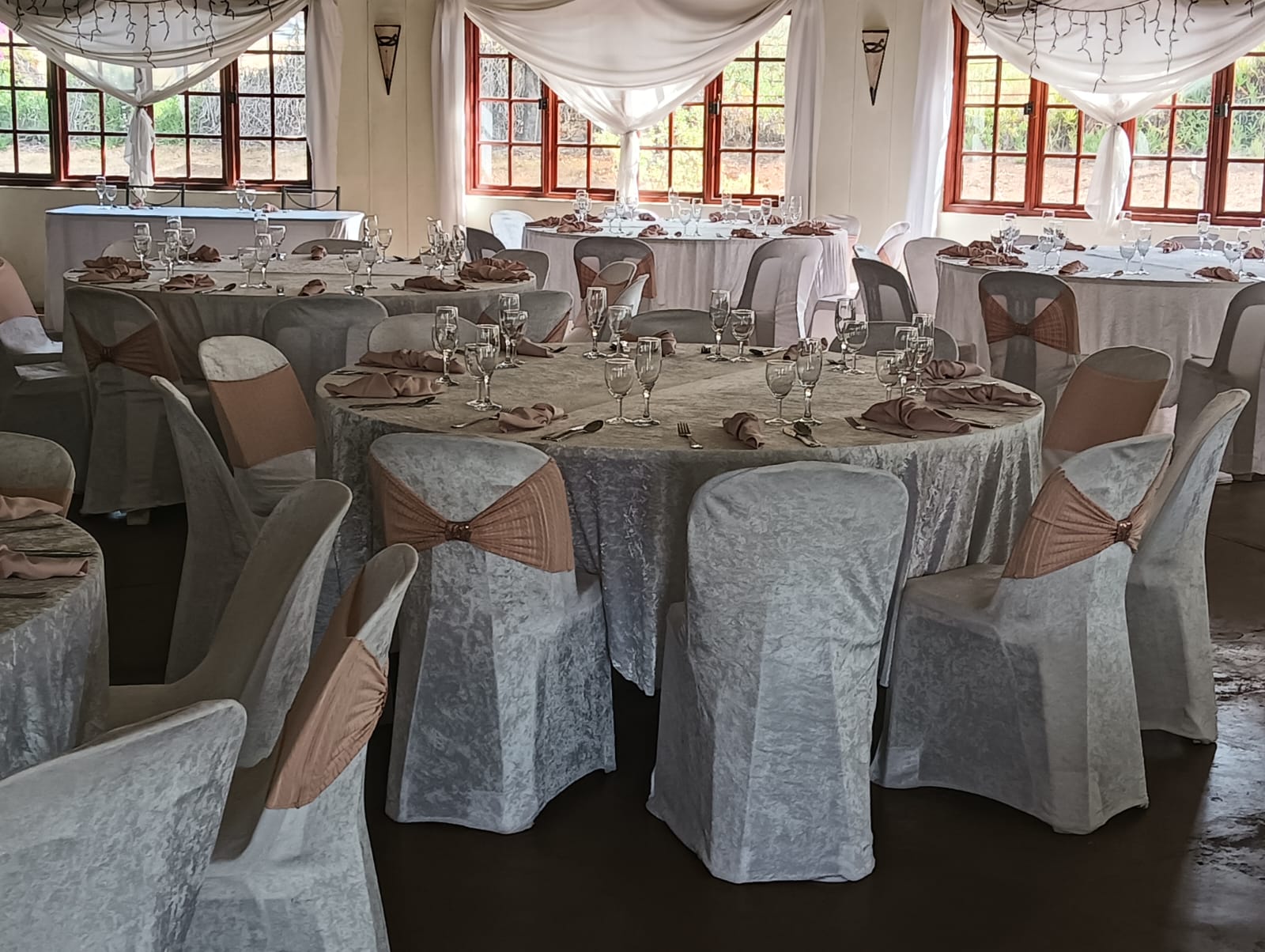 Beautifully set dining tables inside the Mayerskraal wedding and events venue, featuring crisp table linens, glassware, napkins and chair covers with soft draping.