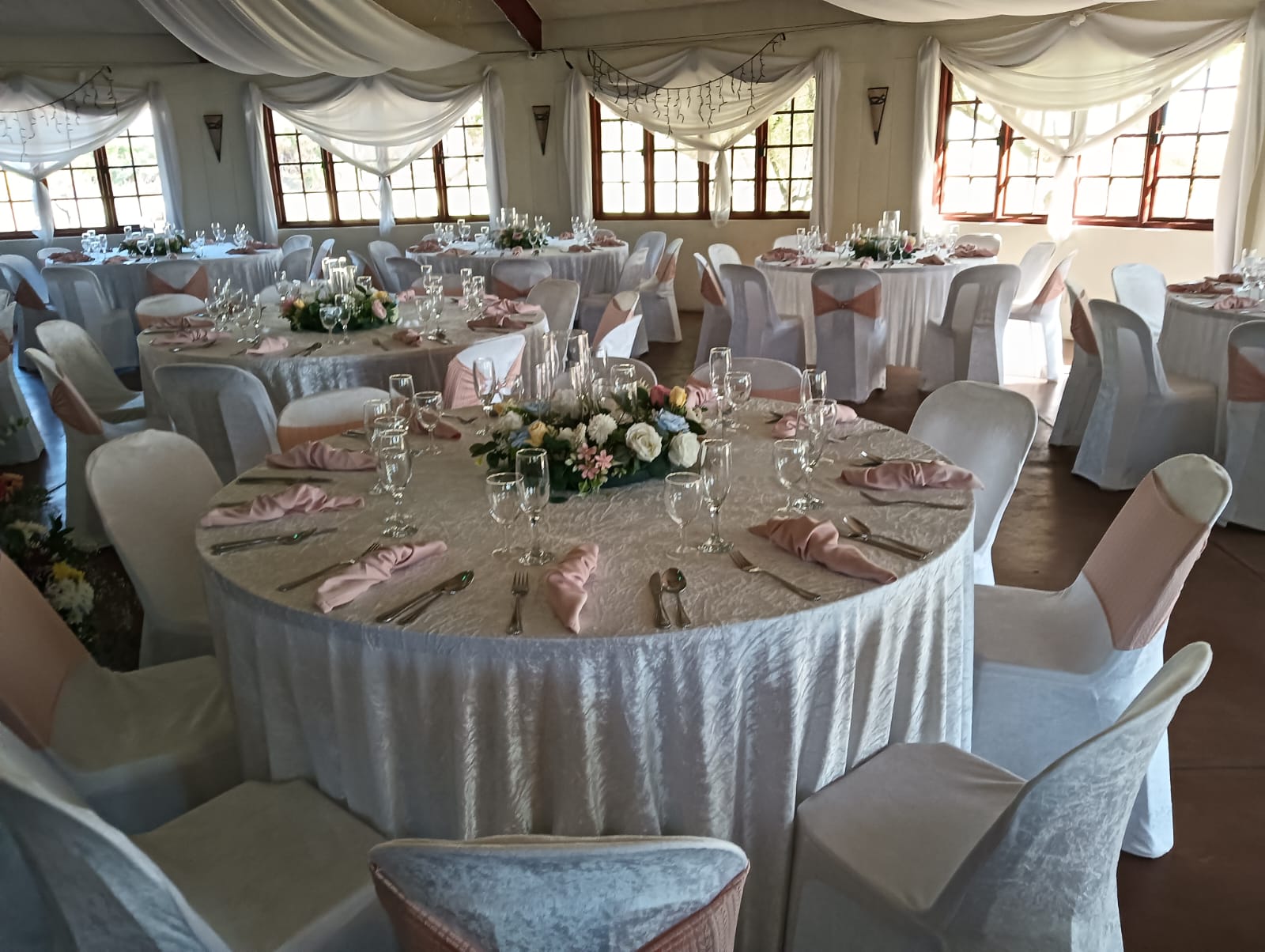 Romantic wedding reception at Mayerskraal featuring round tables with white linens, blush pink napkins, floral centerpieces and white draping.