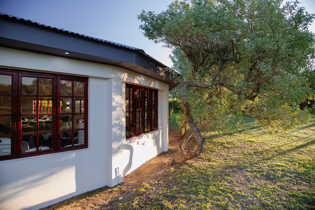 Wedding & Events Venue at Mayerskraal Exterior view of the wedding and events venue at Mayerskraal, featuring large wooden-framed windows, a shaded garden and mature trees.