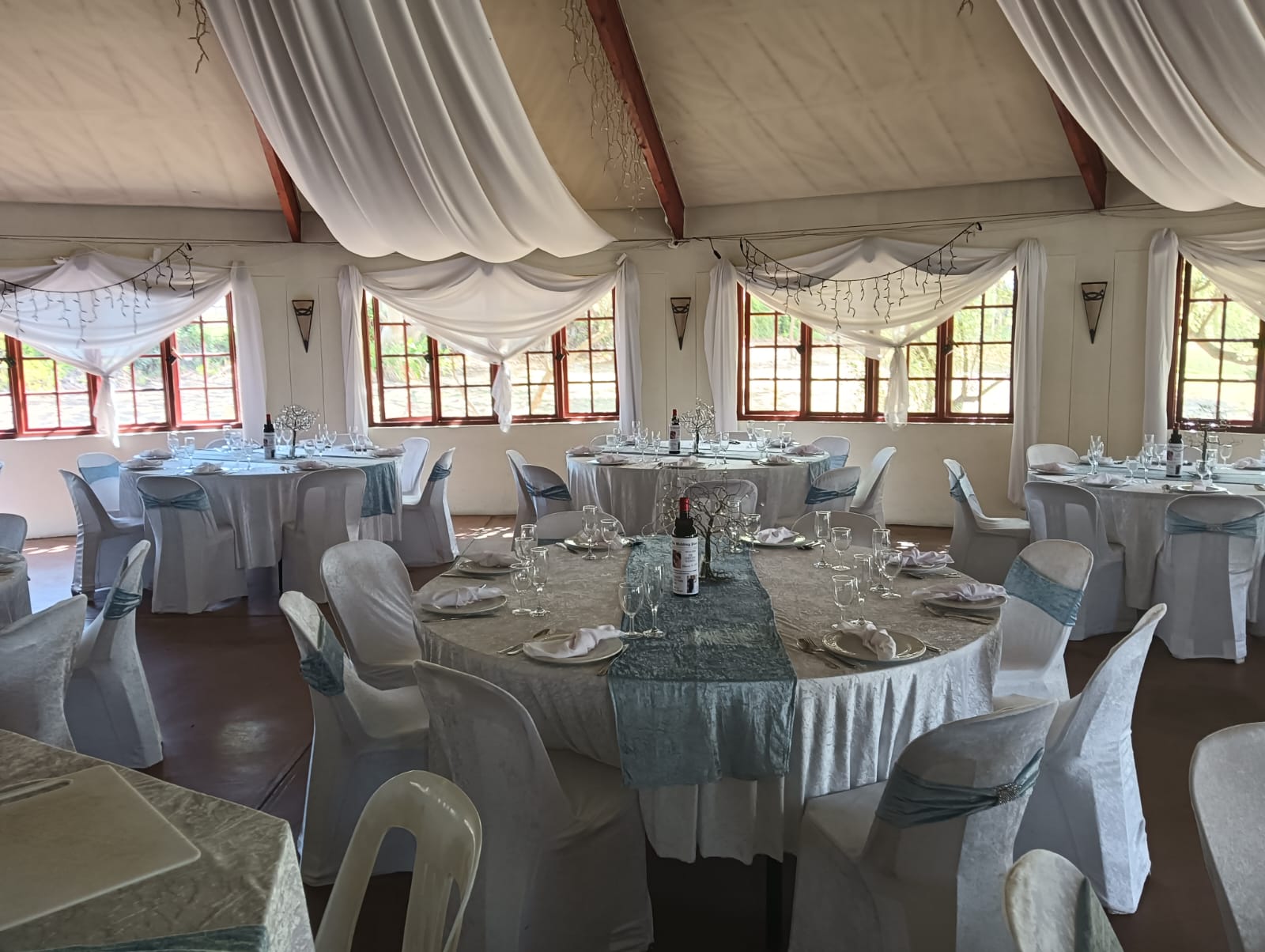 Wedding reception venue at Mayerskraal decorated with white draping, silver-blue table runners, dressed tables and matching chair sashes.