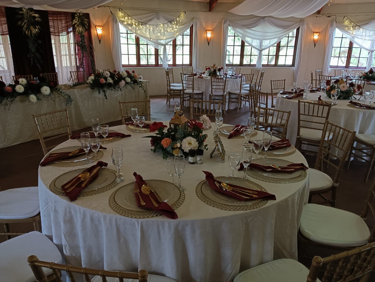 Elegant wedding reception table with floral centerpiece, gold chargers, burgundy napkins and Chiavari chairs at Mayerskraal Wedding Venue