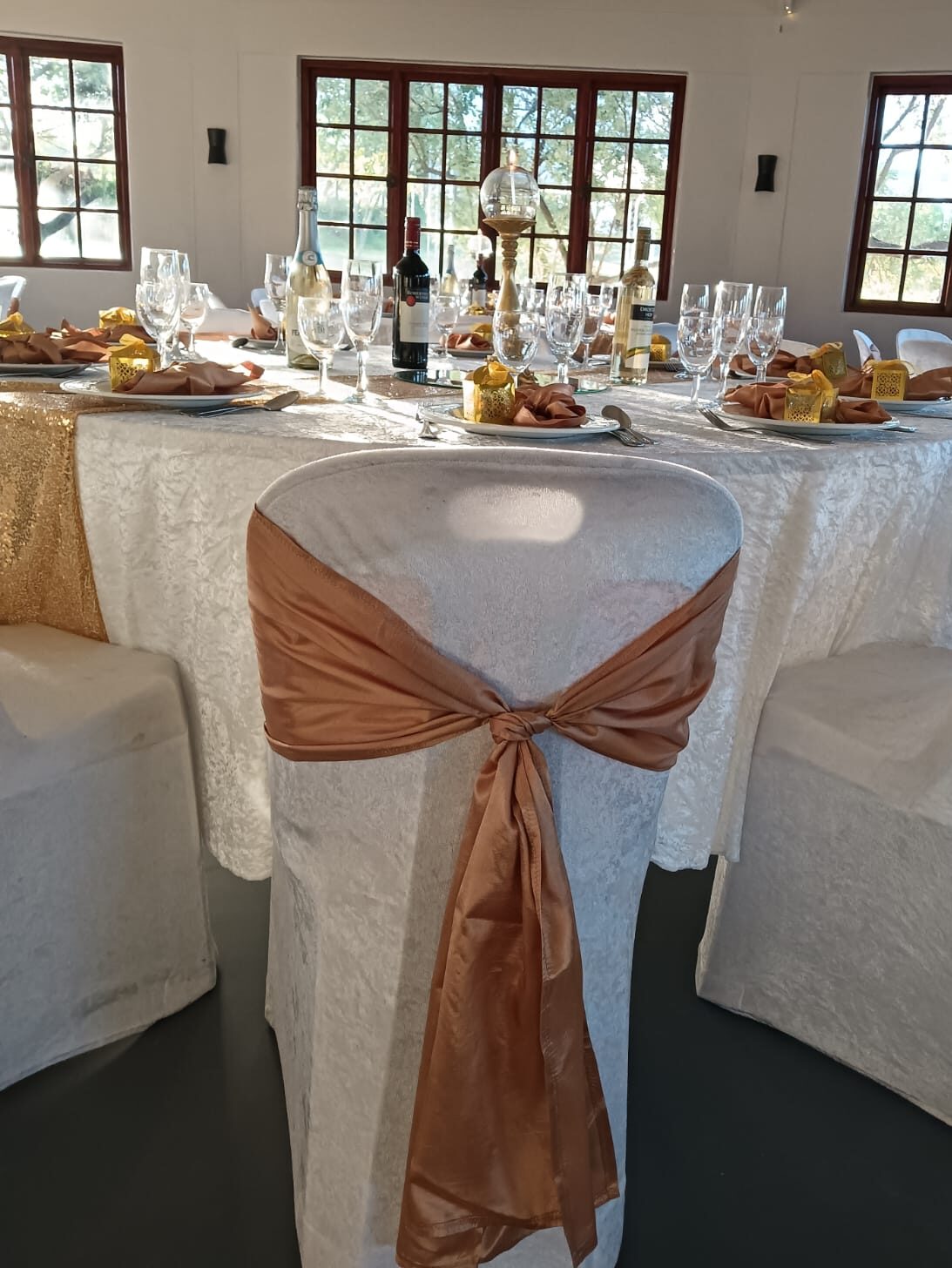 Elegant wedding reception table with white linen, champagne and wine glasses, candles, gold accents and peach chair sashes at Mayerskraal Wedding Venue.